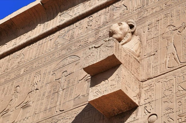 A lion-headed stone water spout projecting from the relief-covered west exterior wall of the Temple of Hathor at Dendera, Egypt.