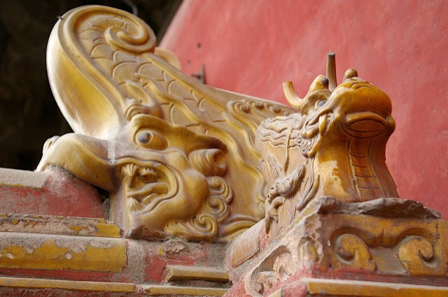 Glazed yellow-tile ridge ornaments on a Forbidden City roof in Beijing: a dragon-headed chiwen with a curled fish tail beside a smaller horned dragon head.