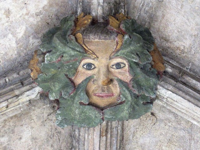 A painted Green Man roof boss, a human face ringed by oak leaves, in the cloisters of Norwich Cathedral.