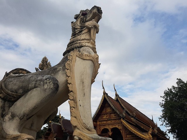 A Lanna-style stone singha lion guardian seen from below against the sky at Wat Chedi Liam in Wiang Kum Kam, Chiang Mai.