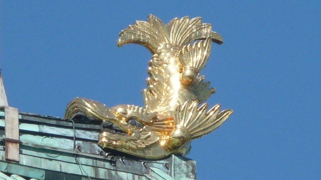 One of the golden shachihoko, the dragon-headed fish ornaments, on a roof of Nagoya Castle in Japan, against a blue sky.