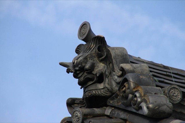 A black glazed-tile onigawara, a fierce horned ogre face, on the ridge end of a roof at Myoshin-ji temple in Kyoto, against the sky.