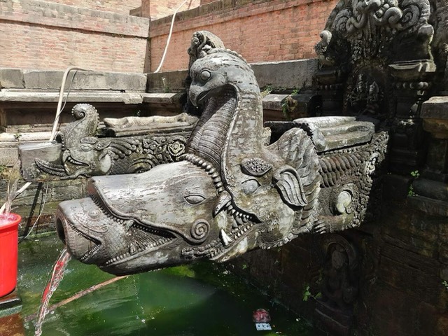 The makara-headed stone spout of Manga Hiti in Patan Durbar Square, Lalitpur, Nepal, in close-up with water running from its mouth.