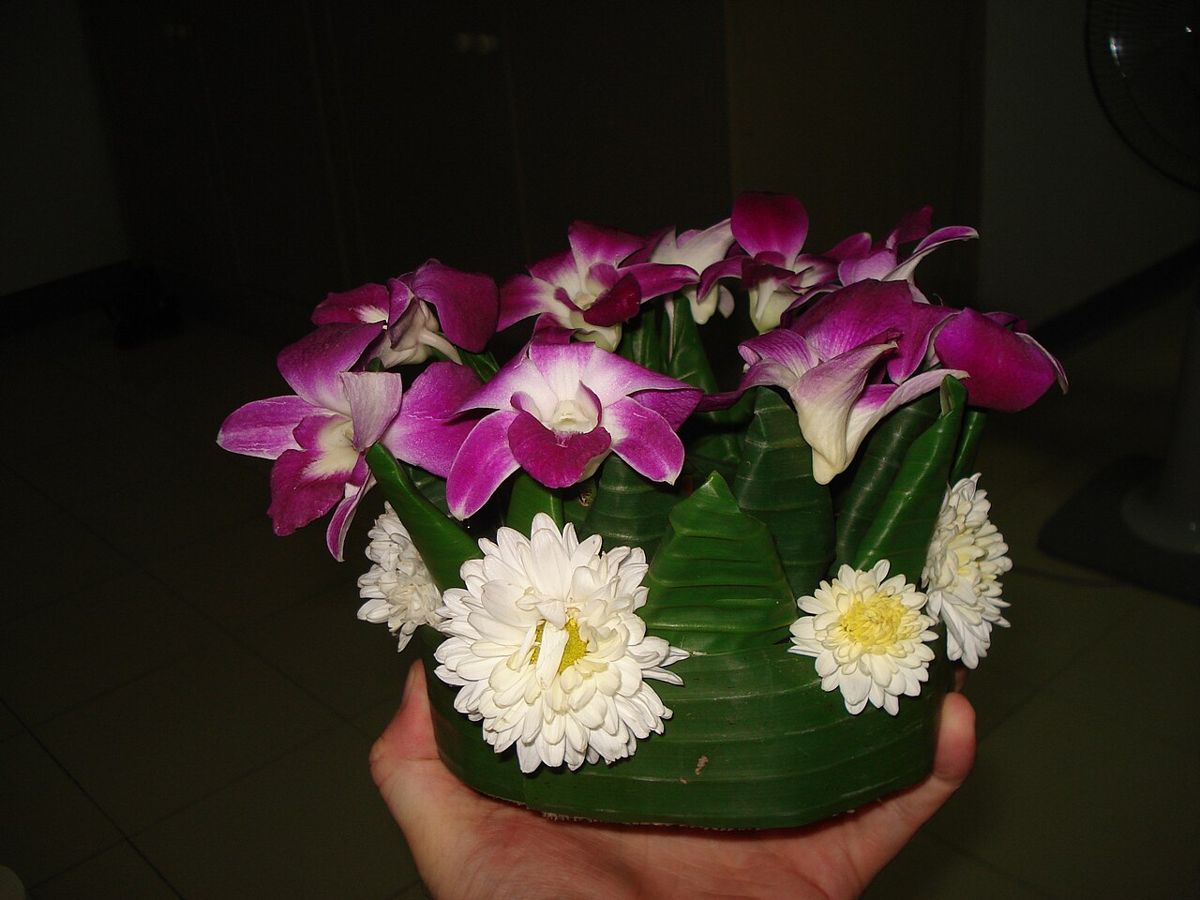 A finished krathong: banana-trunk base, a band of folded leaf petals, orchids and chrysanthemums, pinned together.