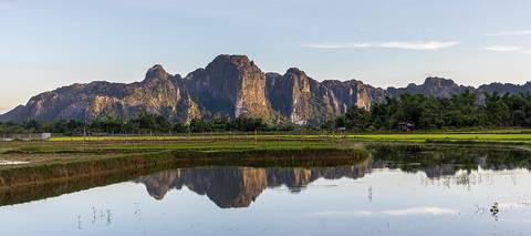Water reflection of karst mountains at golden hour in the countryside of Vang Vieng, Vientiane Province, Laos, during the monsoon.
