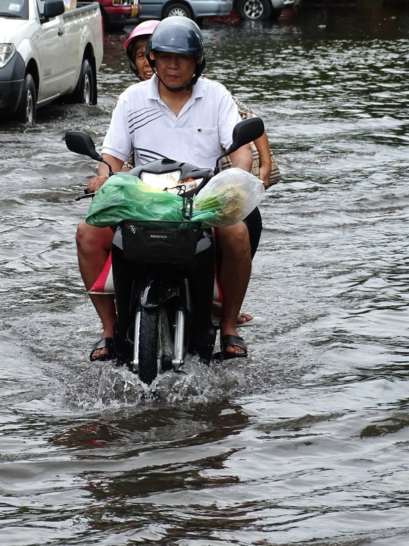 A man rides a motorbike through a flooded Chiang Mai street carrying shopping bags