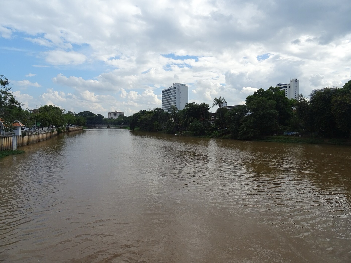 The brown Ping River in flood season between green banks under grey cloud